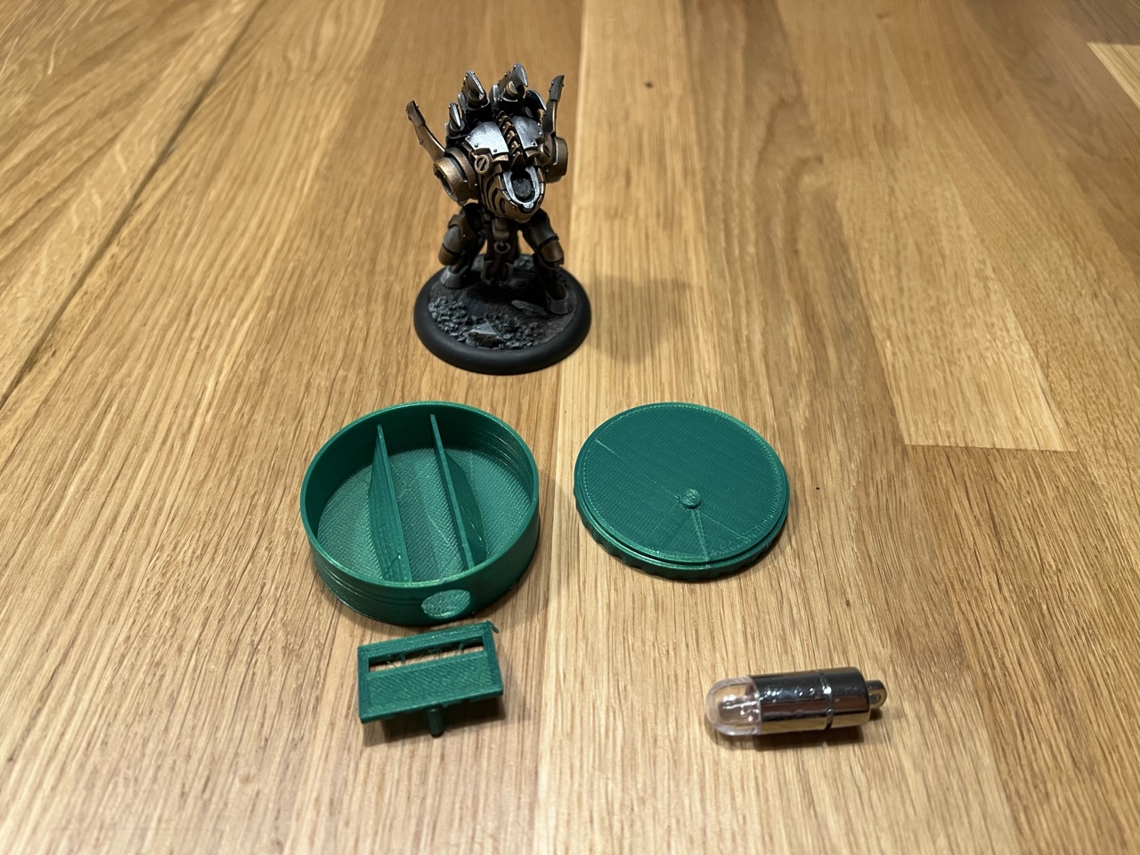 Individual parts of the Beam Base: the base, slider, and top, shown alongside a light source and an RPG miniature.