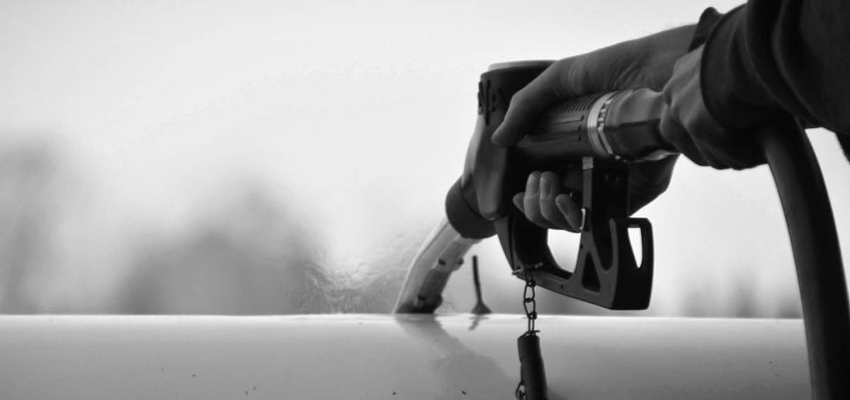 Nozzle of a fuel pump inserted into a fuel tank. Fumes are rising from the tank opening.